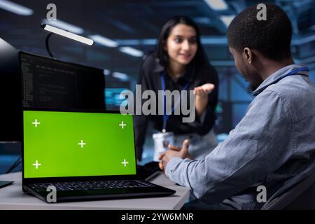 Focus on isolated screen laptop used by team in blurry background reconfiguring server hub to optimize it for data processing. Close up of chroma key notebook used by workers overseeing data center Stock Photo