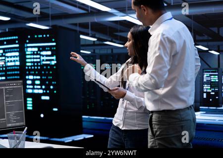 Engineering colleagues in data center looking for firewall misconfigurations affecting servers, doing brainstorming. System administrators in server room checking systems bottlenecks Stock Photo