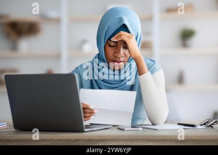 Stressed Black Muslim Woman Working With Papers And Laptop In Office Stock Photo
