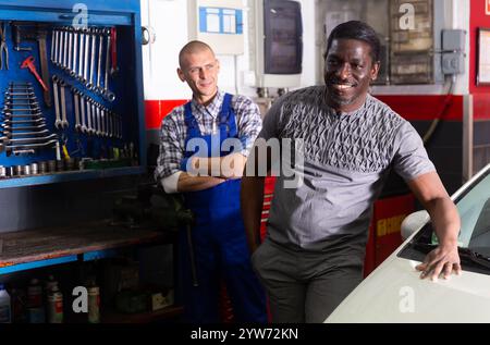 Happy man client with mechanic standing near repaired car Stock Photo