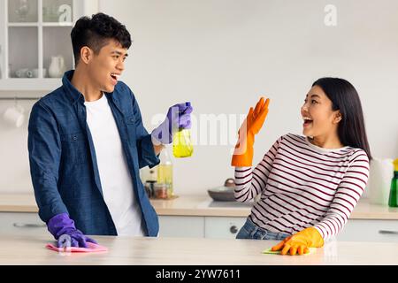 Joyful asian lovers having fun while cleaning kitchen together Stock Photo