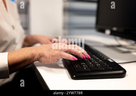 Female hands typing on a black computer keyboard in a modern office.Closeup of female hands using a computer mouse in an office. Stock Photo