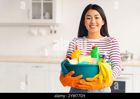 Happy asian woman with cleaning tools standing at kitchen Stock Photo