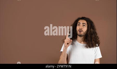 Young man with curly hair gestures upwards in a lifestyle setting Stock Photo