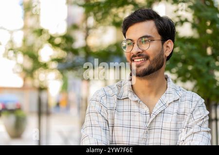 Portrait of happy smiling Indian young man looking at side, resting, relaxation feel satisfied glad expression of good news outdoors. Hispanic guy tourist on urban city street. Town lifestyles. Stock Photo
