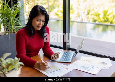 Busness women wearing red sweater working about new startup on smartphone to analysis finance of project in outside office, Woman working using laptop Stock Photo