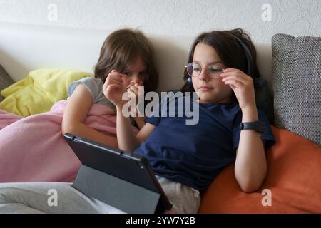 Two sisters lying on the couch looking at the tablet. Concept of children spending time at home Stock Photo