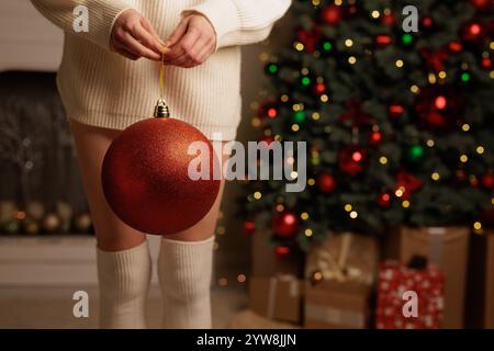 woman holding big red ball christmas tree decoration on background of decorated holiday tree, merry christmas Stock Photo