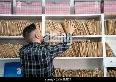 Office worker searching files in archive room, filling cabinet, checking documents, organizing paperwork Stock Photo