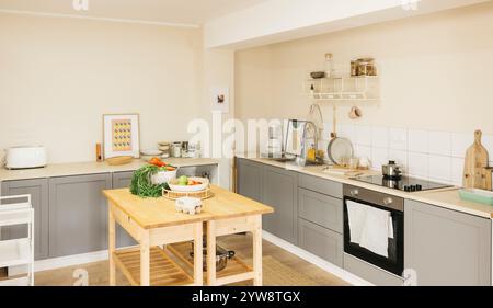 A bright and stylish empty kitchen with fresh vegetables on a central wooden table. Stock Photo
