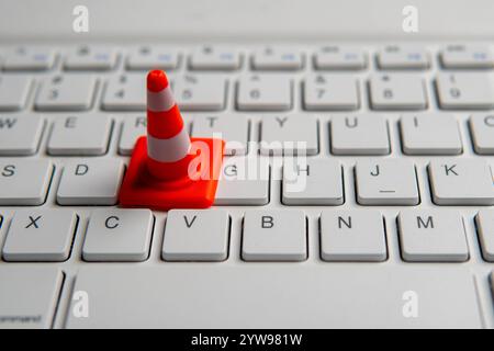 A miniature traffic cone placed on a computer keyboard. Website maintenance, technical difficulties, website under construction concept. Stock Photo