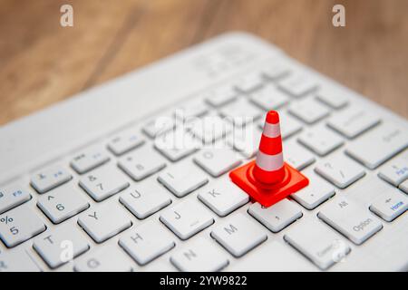 A miniature traffic cone placed on a computer keyboard. Website maintenance, technical difficulties, website under construction concept. Stock Photo