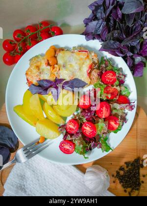 Delicious homemade potato casserole with cherry tomatoes, salad, and basil served on white plate Stock Photo