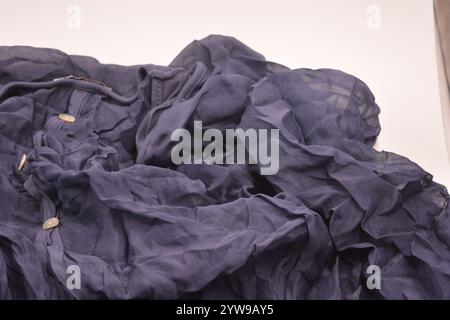 Small white buttons are sewn on an unusual fabric, very crumpled thin as silk, dark blue cotton, viscose is located on a white plastic background. Stock Photo