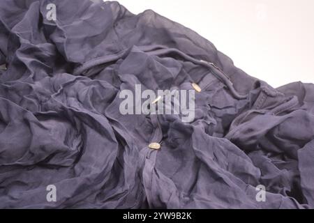 Small white buttons are sewn on an unusual fabric, very crumpled thin as silk, dark blue cotton, viscose is located on a white plastic background. Stock Photo