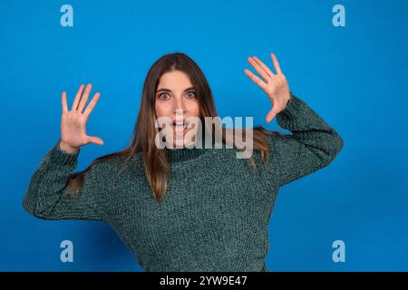 Studio portrait of a surprised young woman gesturing with hands on a vibrant blue background Stock Photo