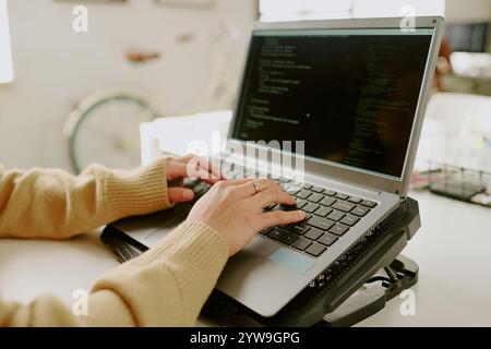 Medium close up of unrecognizable female hand with gold ring typing codes on laptop located on cooling pad Stock Photo