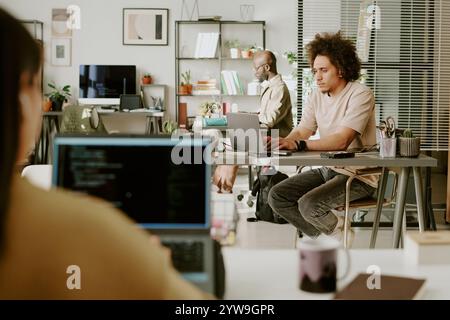 Biracial colleagues sitting at work tables while working via laptops in light modern office, they focused on tasks Stock Photo