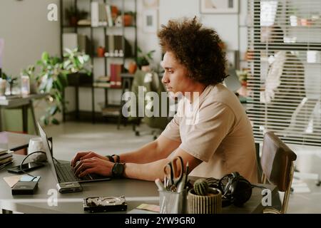 Side view of male biracial worker typing on keyboard while working in office of IT company Stock Photo