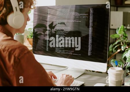 Medium close up of unrecognizable coding and listening to music via wireless headphones Stock Photo