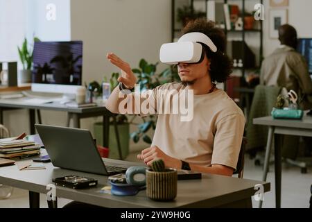 Men with VR headset testing new application and gesticulating wildly while sitting at work desk in office Stock Photo