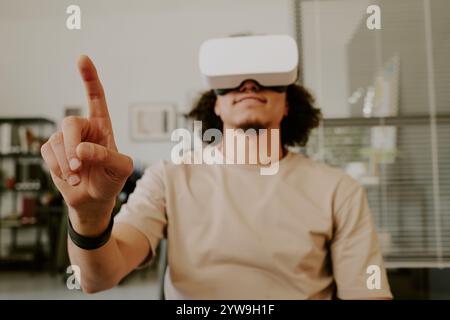 Medium close up of man sitting in office while testing VR headset, focus on hand Stock Photo