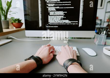 Medium close up of unrecognizable male hands typing codes on white keyboard, computer monitor with codes in blurred background Stock Photo