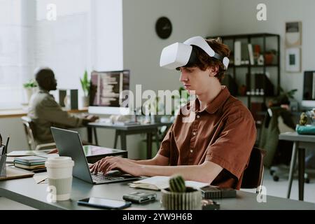 Caucasian man with VR headset sitting at work desk and programming, he focused on process Stock Photo