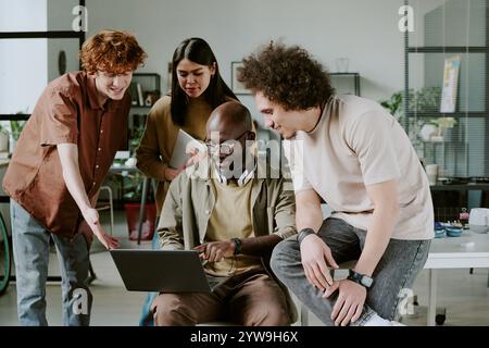Biracial team of young highly skilled programmers looking at screen while discussing new project together in modern office Stock Photo