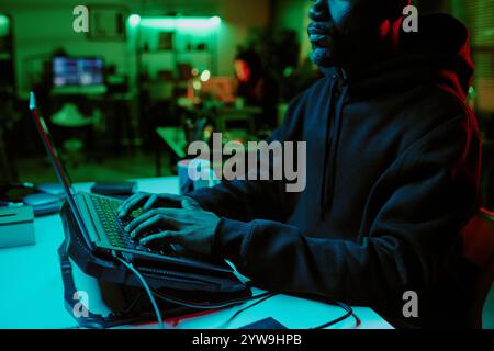 Medium close up of African American hackers hands typing codes on keyboard on laptop on cooling pad Stock Photo