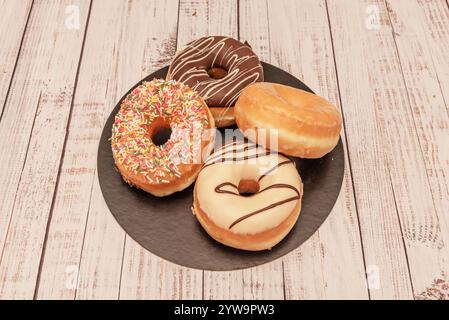 Four donuts of different flavors on a black circular tray Stock Photo