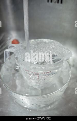 Filling dirty kitchen utensils with running water inside a kitchen sink Stock Photo