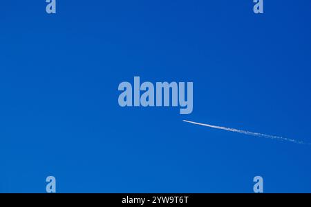Flight of an airplane with a white trail diagonally against a clear blue sky. For text. Stock Photo