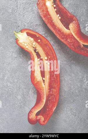 Fresh red peppers are sliced to reveal their bright interior, showcasing seeds and texture. The vibrant colors contrast against a smooth gray backgrou Stock Photo