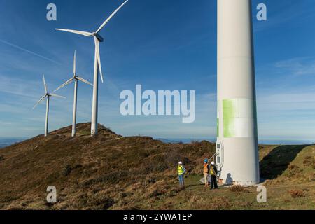 Three engineers engaged in discussion near the base of a wind turbine, collaborating on green energy production under a bright blue sky on a sunny day Stock Photo