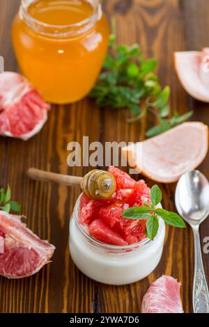 homemade sweet yogurt in a glass jar with pieces of red ripe grapefruit and honey, on a wooden table . Stock Photo