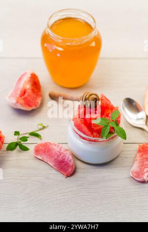 homemade sweet yogurt in a glass jar with pieces of red ripe grapefruit and honey, on a wooden table . Stock Photo