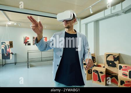 Young man in elegant blue suit and VR headset looking through interactive list of modern art exhibition Stock Photo