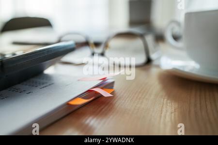 colorful paper marks in documents close-up, Eyeglasses and calculator in backdrop with white tea cup on accountant desk next bright daylight window. B Stock Photo