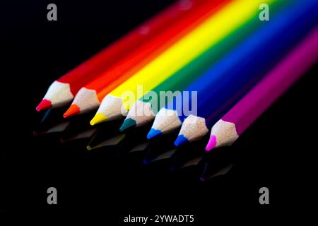 A row of coloured pencils on a reflective black surface Stock Photo