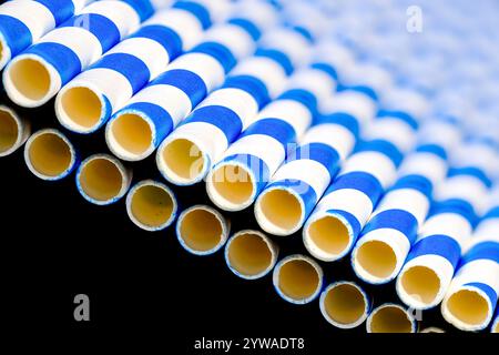 A row of blue and white, paper drinking straws, laying on a reflective black surface Stock Photo