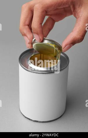 hand opening yellow adhesive in silver tin can isolated gray background, mock-up template of synthetic glue metal container with blank label Stock Photo