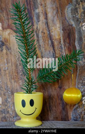 two fir fronds with single cheap hanging bauble sat in smiley face egg cup concept budget cost of living crisis christmas tree decoration Stock Photo