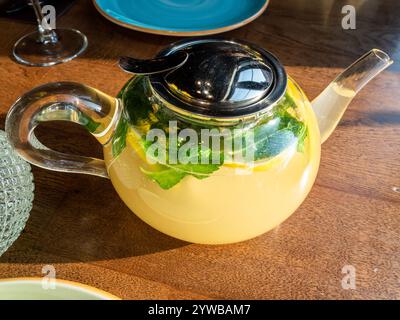 glass teapot with mint, ginger tea with lemon illuminated by sun light on table Stock Photo