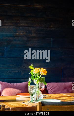 fresh yellow roses in glass vase illuminated by sun on table in restaurant Stock Photo
