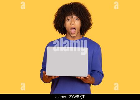Young man surprised using a laptop on a bright yellow background Stock Photo