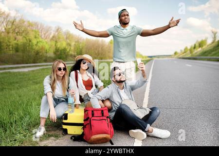 Unhappy millennial tourists sitting on roadside, cannot catch car, waiting for too long, having no smartphone connection Stock Photo