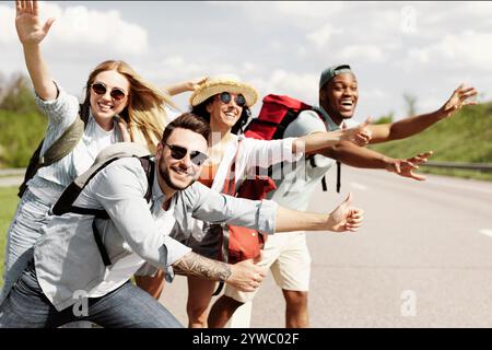 Cheerful young people standing on roadside, stopping car, trying to get free ride, having autostop journey, free space Stock Photo