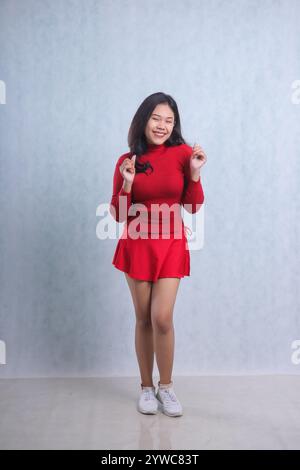 full length Asian ladies wearing red sweater, standing cheerful looking at camera both hands clenched in a sign of success, isolated on white backgrou Stock Photo