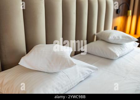 Szklarska Poreba, Poland - May 20 2024: Two stacks of white pillows lying on large bed with decorative headrest on wall and small lights on both sides Stock Photo